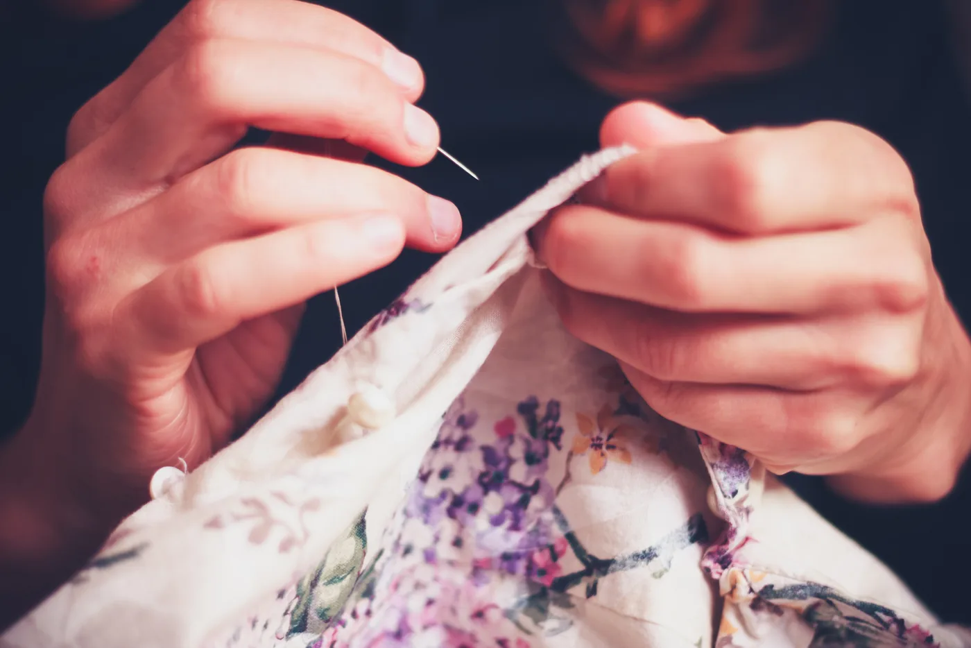 Mãos costurando à mão um tecido claro estampado de flores lilases